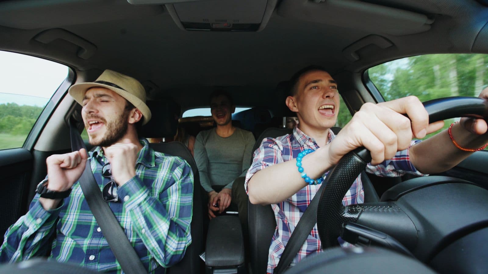 Dos amigos cantando adelante en un auto, con una tercera persona en el asiento de atrás
